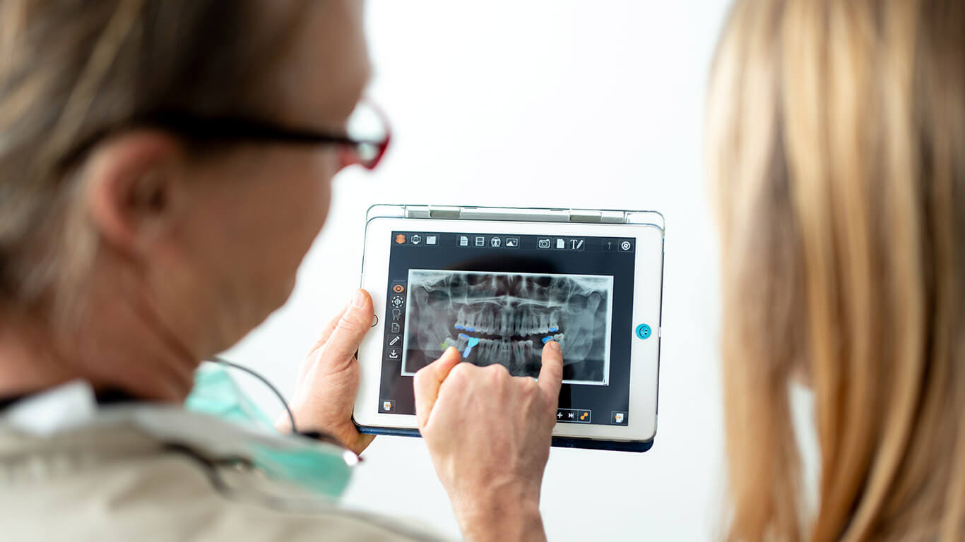 Arzt zeigt Patientin ein Röntgenbild des Kiefers auf dem IPad