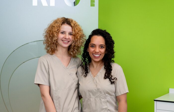 Zwei Zahnärztinnen lachen im Praxisraum in die Kamera