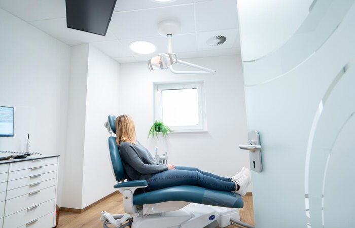 Blonde Patientin sitzt auf Zahnarztstuhl und blickt aus dem Fenster