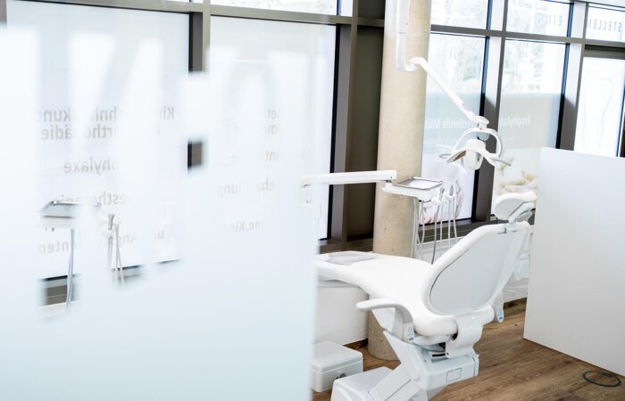 Zahnarztstuhl im Behandlungsraum Kieferorthopädie vor Glastür mit Milchglasfolie